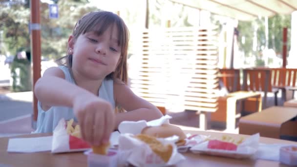 街头食品，漂亮的小女孩在街上的咖啡店里吃快餐 — 图库视频影像