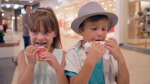 Édesszájú, boldog gyerekek barátok sütit és fánkot esznek a bevásárlóközpontban — Stock videók