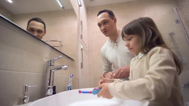 Kinder Morgenhygiene, junger Vater bringt Tochter bei, Zähne zu putzen und Mundgesundheit vor Spiegel über Waschbecken zu überwachen — Stockvideo