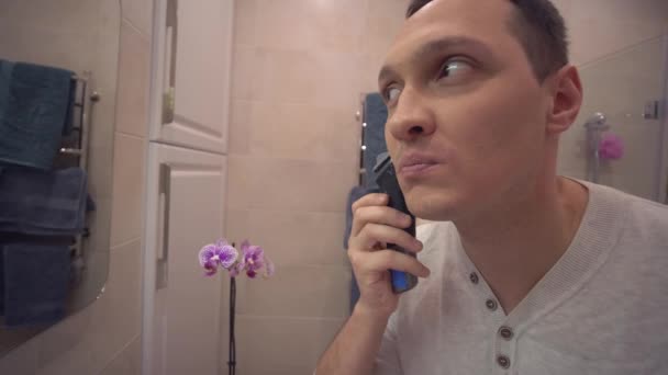 남성아름다움 관리 일상 생활, 전기 면도칼을 사용하는 성인 남성 화장실에서 거울 앞에서 수염을 깎는 모습 — 비디오