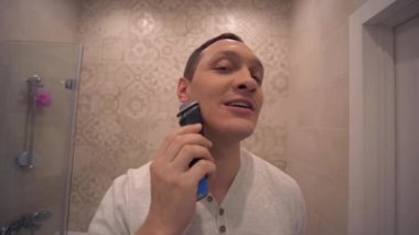 Elektrikli Usturalı olgun yakışıklı adam banyoda aynanın önünde sakallarını tıraş eder.