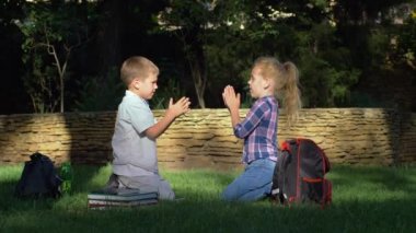 Mutlu okul çocukları okul tatilinde öğrendikten sonra çimenlerde oturup el çırpma oyunu oynuyorlar.