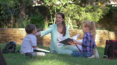 Açık hava dersi, mutlu sınıf arkadaşları. Eğitimci kız ve erkek öğrenciler. Ders sırasında kitap okuyup sohbet ediyorlar.