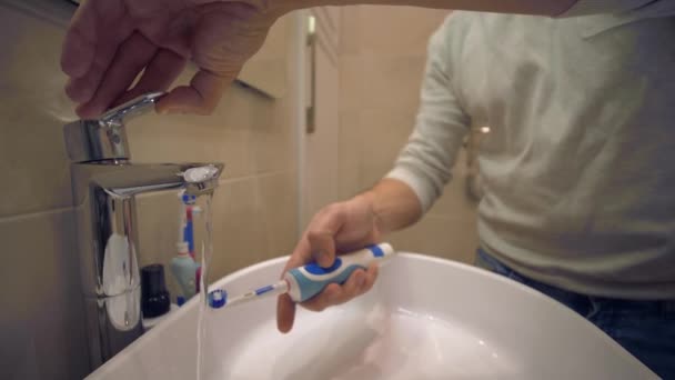 Rutina de la mañana, manos masculinas colocar pasta de dientes en el cepillo de dientes para cepillar los dientes sobre el fregadero en el baño — Vídeo de stock