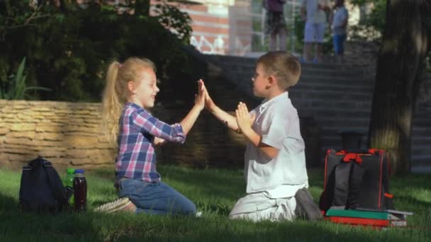 Niños felices jugando juego de aplausos sentado en la naturaleza después de las lecciones sobre las vacaciones escolares — Vídeos de Stock