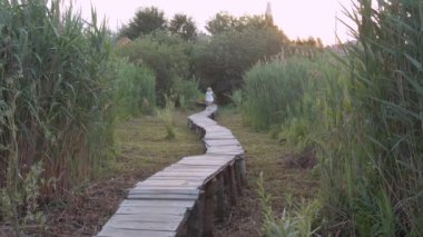 Beyaz elbiseli küçük güzel kız yeşil çimenlerin arasında ahşap köprü boyunca koşuyor.