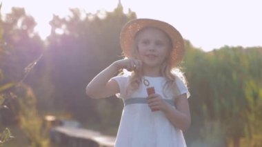 Hasır şapkalı neşeli, güzel, gülümseyen küçük kız köpükler saçar ve güneşli ışıkta güler.