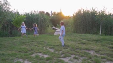 Mutlu arkadaşlar, neşeli aktif çocuklar oğlanlar ve kızlar yetişip güneşin altında yeşil çimlerde koşuyorlar.