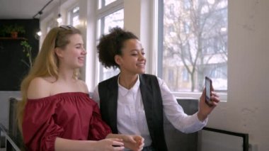 Uluslararası dostluk, neşeli çoklu etnik kız arkadaşlar, akıllı telefondayken selfie çekiyorlar.