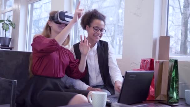 Vidám sötét bőrű serdülő lány számítógép laptop és kaukázusi barátnője Vr headset játék virtuális valóság ül a kávézóban — Stock videók
