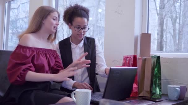 Internet köp, glada afrikanska amerikanska flicka med vän använda modern teknik för att betala online inköp sitter i café med många shoppingväskor — Stockvideo