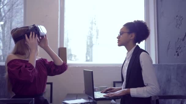 Виртуальная реальность игры, счастливые смешанные расы друзья девушки используют VR гарнитуры и современные технологии ноутбука для игры виртуальной реальности сидя в помещении — стоковое видео