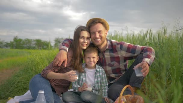 Családi idill, mosolygós anya apa és fia ölelés közben pihentető piknik a természetben a zöld mezőn — Stock videók