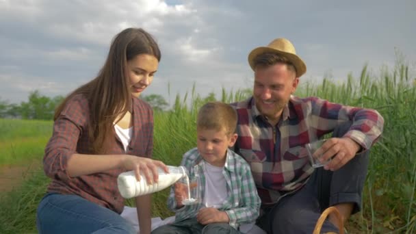 Familia rural, mujer feliz verter leche en el vaso para el hijo y el marido durante el picnic en la naturaleza en el campo de grano — Vídeo de stock