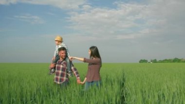Aile huzurlu, mutlu, genç bir çift. Omuzlarında çocuk, yeşil alanda gökyüzüne karşı yürüyor.