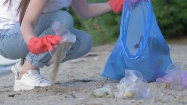 Doğa ekolojisine dikkat et, lastik eldivenli gönüllü kız deniz kenarını temizlerken çöp torbasında plastik çöp topluyor.