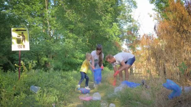 Vård natur ekologi, ung familj av aktivist med unge flicka samlar skräp i papperskorgen medan rengöra naturen från plast och polyeten — Stockvideo