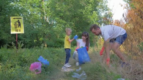 Het plukken van afval, jonge man en vrouw met kind meisje geeft om ecologie milieu en het verzamelen van plastic afval in vuilniszak tijdens het reinigen van vervuiling — Stockvideo