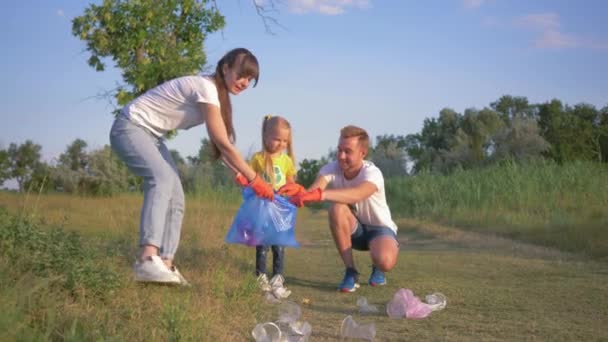 Porträtt av ung lycklig familj av aktivist med unge flicka samlar avfall i papperskorgen medan rengöring av naturen från plast och polyeten — Stockvideo