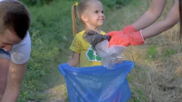 Врятувати планету, молоду сім'ю з щасливою милою дівчинкою в гумових рукавичках збирає відмову в мішку для сміття на природі з пластику — стокове відео