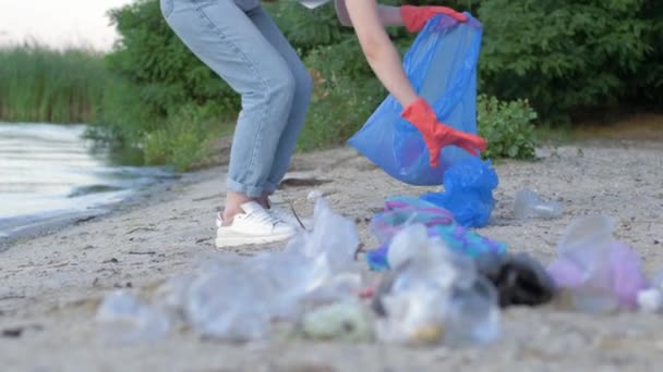 Limpeza de praia, ativista fêmea em luvas de borracha coleta resíduos de plástico em saco de lixo enquanto limpa aterro — Vídeo de Stock