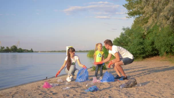 Καθαρίζοντας τη φύση, η νεαρή οικογένεια εθελοντών με παιδί συλλέγει σκουπίδια σε σακούλα σκουπιδιών ενώ καθαρίζει την παραλία από πλαστικό και πολυαιθυλένιο — Αρχείο Βίντεο