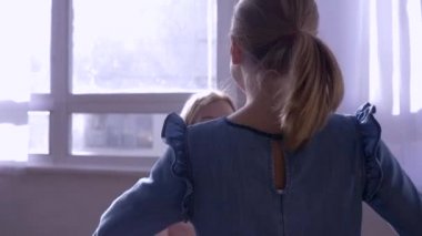 Anne kucağı, küçük kız annesinin kollarına koşar ve güneş ışınlarının penceresine karşı kocaman bir kucaklama yapar.