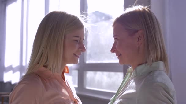 Материнские ценности, счастливая мама с дочерью, чтобы обнимать головы друг с другом в подсветке в комнате напротив окна — стоковое видео