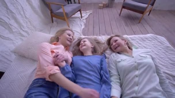 Komik bir aile, mutlu bir anne, yetişkin ve küçük bir kızı olan mutlu bir anne eğlence sırasında yatağa düşüyor. — Stok video