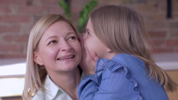 Szczęśliwe macierzyństwo, małe uśmiechnięte dziecko dziewczyna mówi ukochanej mamie szepcząc sekrety w uszach w domu — Wideo stockowe