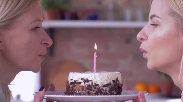 Fazer desejo no aniversário, mãe feliz com a filha adulta soprando velas no bolo de férias e sorrisos e olhar um para o outro — Vídeo de Stock