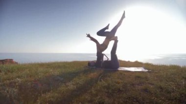 Yoga, atletik kadın akrobat erkek ortağının elleri ve bacakları üzerinde dengede duruyor. Gökyüzünün arka planında ve dağdaki denizde.