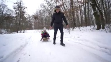 Karlı ormanda mutlu bir aile, baba oğlunu ve kızını kışın kızağa çekiyor.