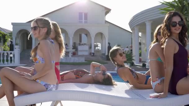 Dziewczyny na letnim odpoczynku, atrakcyjne Przyjaciółki w strojach kąpielowych i okularach jednocześnie kładą się na leżaku przy basenie — Wideo stockowe