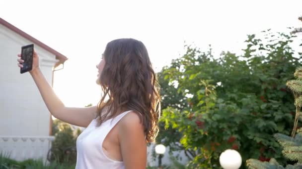 Mooie vrouw doet selfie foto op mobiele telefoon in felle zonnestralen buiten — Stockvideo