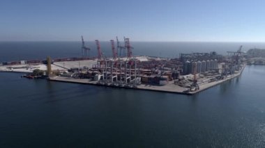 Konteynırlı ticari liman ve deniz kıyısındaki vinçleri mavi gökyüzüne ve parlak suya karşı kaldırmak