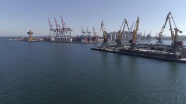 Deniz endüstrisi, konteynırları olan ticari liman ve deniz kıyısında mavi gökyüzüne ve parlak suya karşı vinçleri kaldırmak.