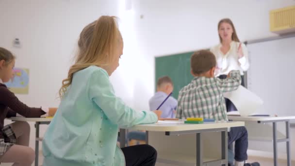 Portret van een schoolkind aan een bureau tijdens een les in een klaslokaal op de basisschool zonder gerichte achtergrond — Stockvideo