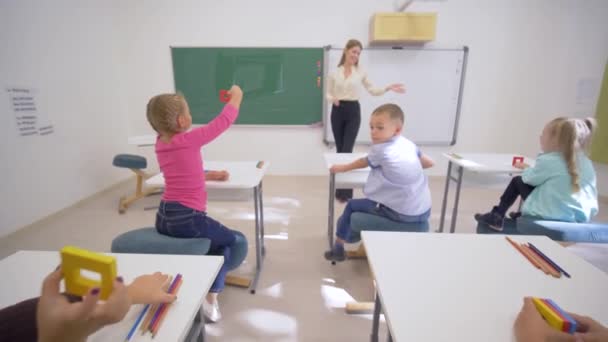 Děti školné, veselá pedagožka žena v blízkosti palubě provádí kognitivní lekce pro roztomilé žáky na stole ve třídě školy — Stock video