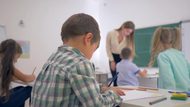 Porträt eines lächelnden Schülers am Schreibtisch während des Unterrichts im Klassenzimmer der Grundschule auf unfokussiertem Hintergrund — Stockvideo