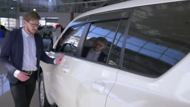 Concesionario de automóviles, hombre comprador dichoso en gafas con el disfrute acariciando el nuevo vehículo sonriendo suavemente en el centro de venta de automóviles — Vídeos de Stock