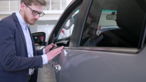 Sala de exposición de coches, feliz comprador chico gafas con placer acariciando nueva máquina suavemente sonriendo en Auto centro de venta — Vídeo de stock