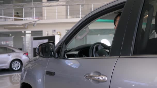 Счастливый владелец нового авто, улыбающийся потребитель азиатская женщина показывает ключи, сидя в салоне и подглядывая в окно в дилерской — стоковое видео