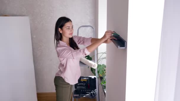 Επιδιόρθωση διαμέρισμα, όμορφη γυναίκα κάνει ανακαίνιση και κρεμάει ράφι στον τοίχο κατά τη διάρκεια της ανακαίνισης του σπιτιού — Αρχείο Βίντεο