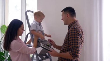 İç dekorasyon sırasında yeni dairede mutlu bir aile, neşeli bir baba oğluyla oynuyor ve karısı kocasını öpüyor.