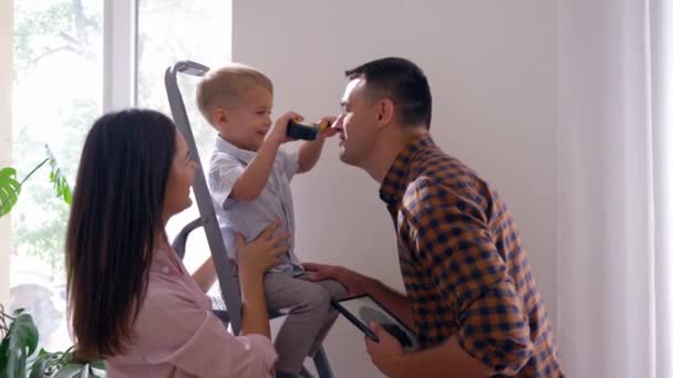 Jong gezin met kleine zoon doet reparaties en opknoping plank aan de muur in huis — Stockvideo