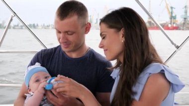 Baba sütle beslenir küçük bir çocuk ellerinde küçük bir şişeyle, ailesi tatilde, ebeveynleri ve çocukları denizde