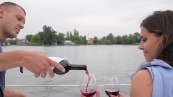 Guy pours from bottle wine, romantic couple drink red beverage on sea, two people on vacation, glasses in hands man — Stock Video