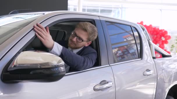 Πορτρέτο του χαρούμενου αγοραστή αυτοκινήτων, ο πελάτης απολαμβάνει το νέο αυτοκίνητο και παρουσιάζει τα κλειδιά που κάθονται στην καμπίνα και κοιτάζοντας μέσα από το παράθυρο στο σαλόνι αυτοκινήτων — Αρχείο Βίντεο