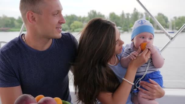 Genitori con bambino su yacht, bambino mangia il primo cibo sulle mani mamme a riposo, coppia d'amore insieme con piccolo bambino — Video Stock